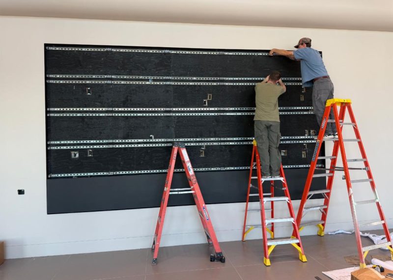 Installation visualization showing two installers on ladders aligning a StrutWall video wall frame.